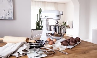 Valkoinen yleiskone keittiön työtasolla, jonka vieressä valmiita muffinsseja, ja leivontatarvikkeita
