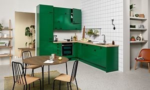 Vihreä EPOQ Trend -keittiö L-mallisena, integroidulla uunilla sekä puukuvioisella työtasolla, etualalla ruokailuryhmä
