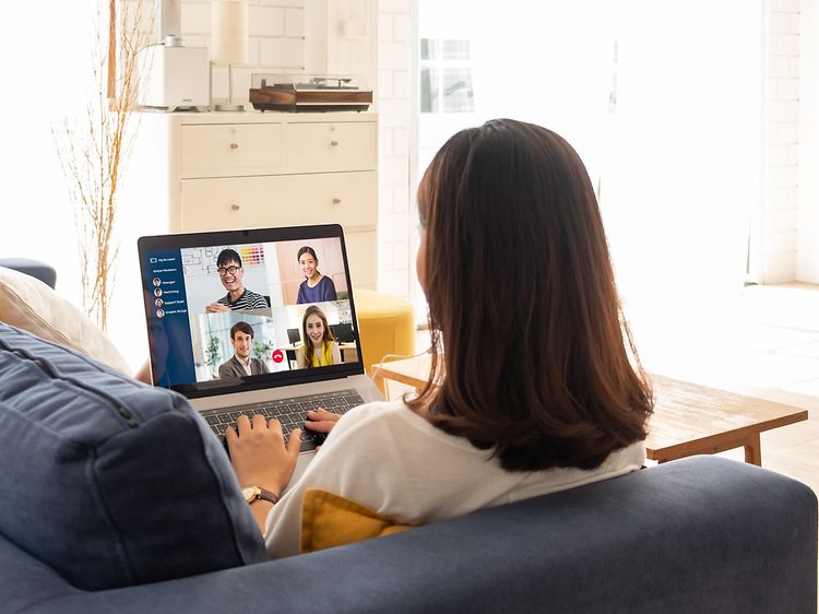 Woman sitting on couch while attending a meeting on her laptop