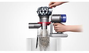 Henkilö tyhjentää Dyson V8 -pölynimurin pölysäiliötä