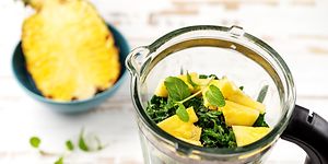 Tehosekoitin, jossa on yrttejä ja leikattuja ananaspaloja sekä puolikas ananas tehosekoittimen vieressä