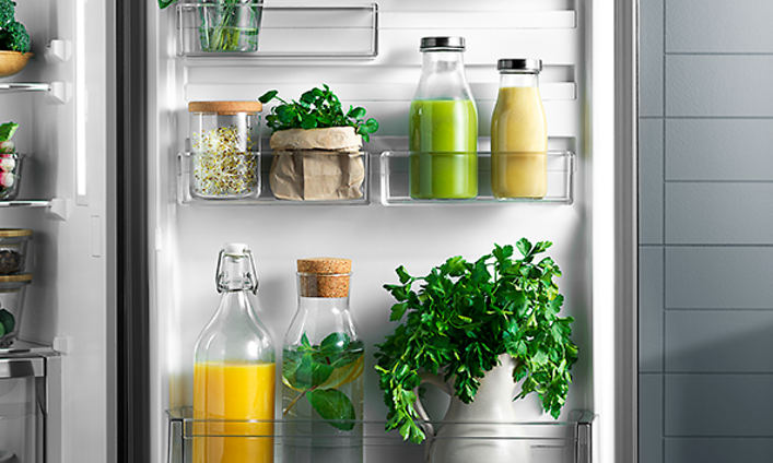 Avoin Electrolux-jääkaappi ja sen sisällä apelsiinimehua, vihersmoothieta ja tuoreita yrttejä
