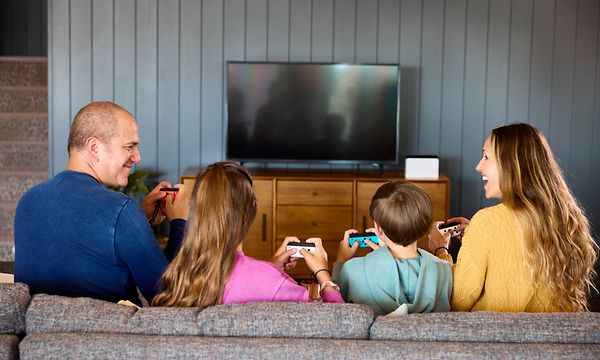 Nelihenkinen perhe pelaa Nintendo Switchiä sohvalla