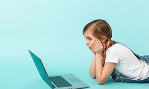 Tyttö kannettavan tietokoneen edessä lattialla mahallaan