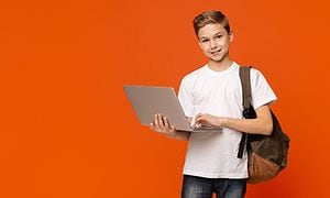 Reppu selässä oleva poika pitelee kannettavaa tietokonetta