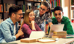 Neljä opiskelijaa kerääntyneenä kannettavan ympärille ja vieressä erilaisia kirjoja pöydällä