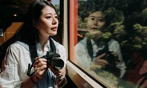 Nainen katsoo ulos junan ikkunasta järjestelmäkamera kädessään