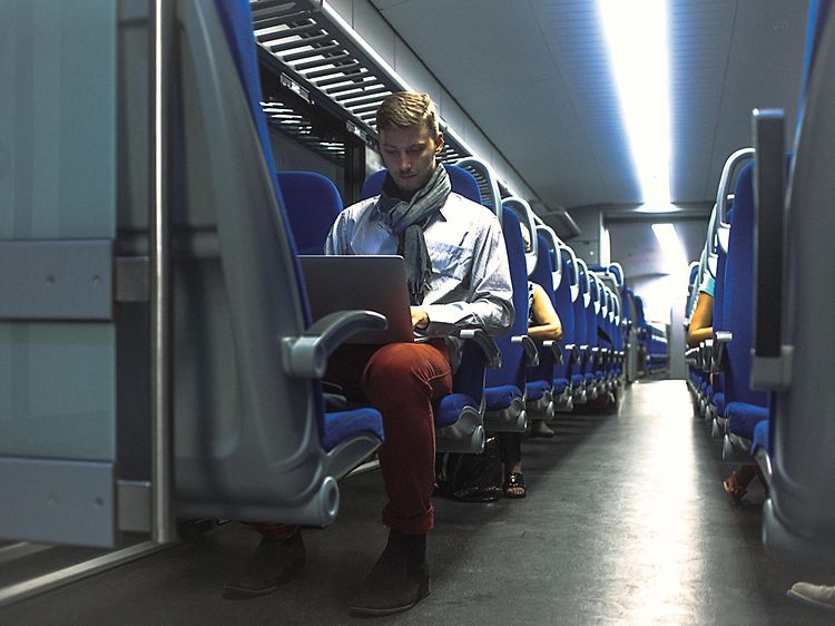 Mies työskentelee kannettavalla tietokoneella matkustaessaan töihin
