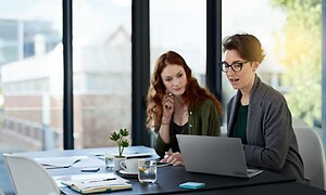 Kaksi naista toimistolla ja kannettava tietokone