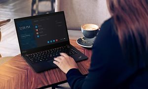 Nainen istuu kahvilassa nauttimassa kahvia ja työskentelee Lenovo ThinkPad-kannettavalla