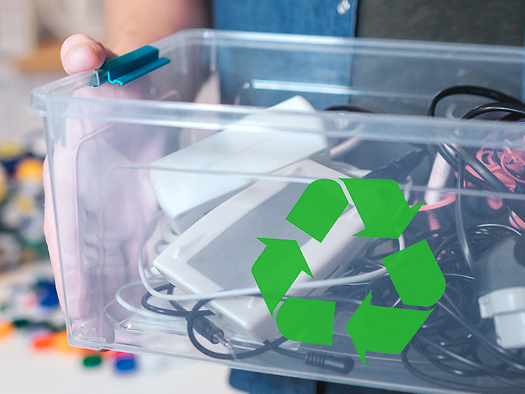 Mies pitelee laatikkoa jossa vanhaa elektroniikkaa ja kierrätyssymboli