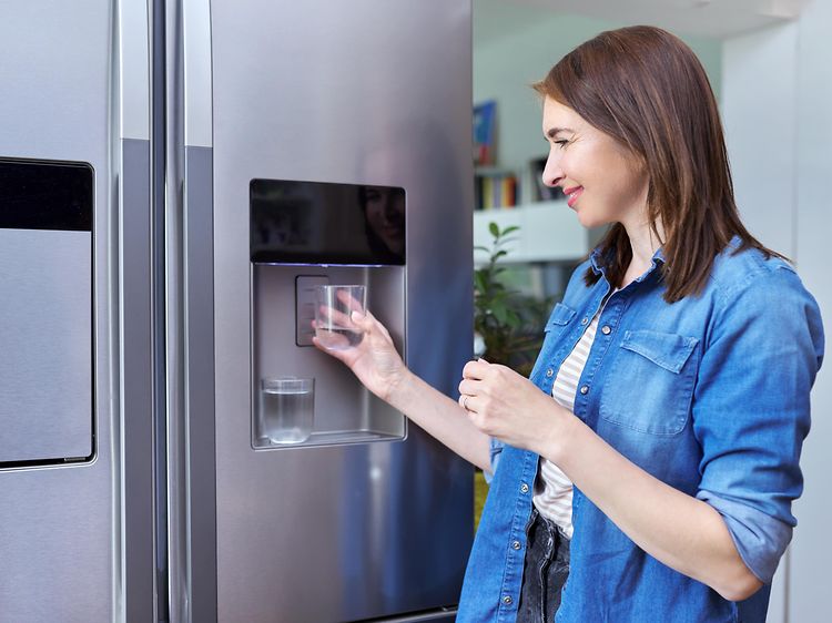 Nainen ottaa jääkaapin jääpalakoneesta jäätä lasiinsa