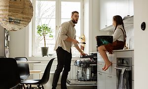 Mies laittaa ruokailuvälineitä astiapesukoneen erilliselle aterintasolle