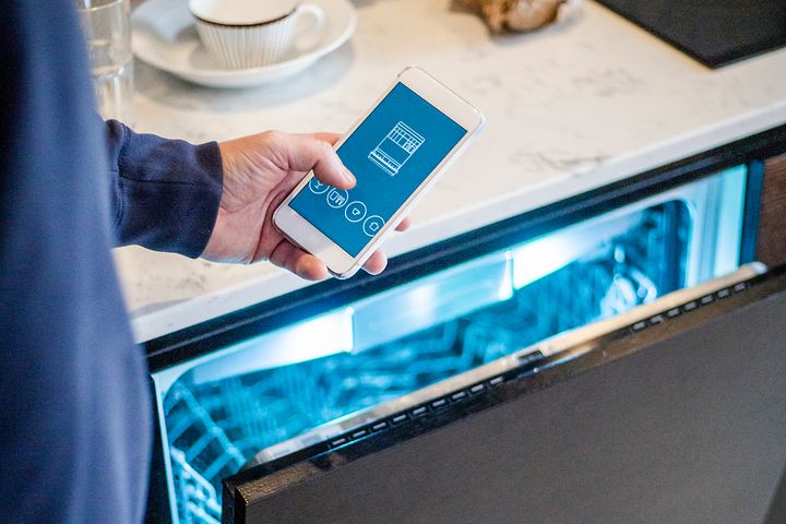 Mies pitelee puhelinta avoinna olevan astianpesukoneen edessä