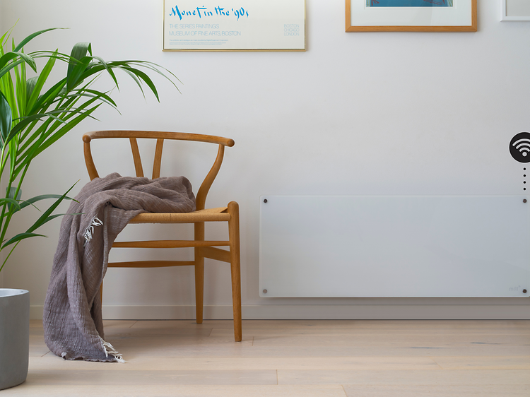 Valkoinen älylämmitin seinällä sekä WiFi-symboli ja puinen tuoli ja viherkasvi