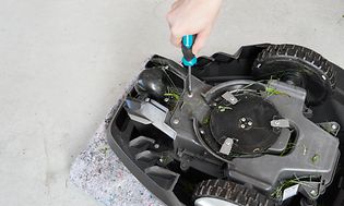 Robottiruohonleikkuri ylösalaisin ja käsi ruuvaamassa sen pohjaa ruuvimeisselillä