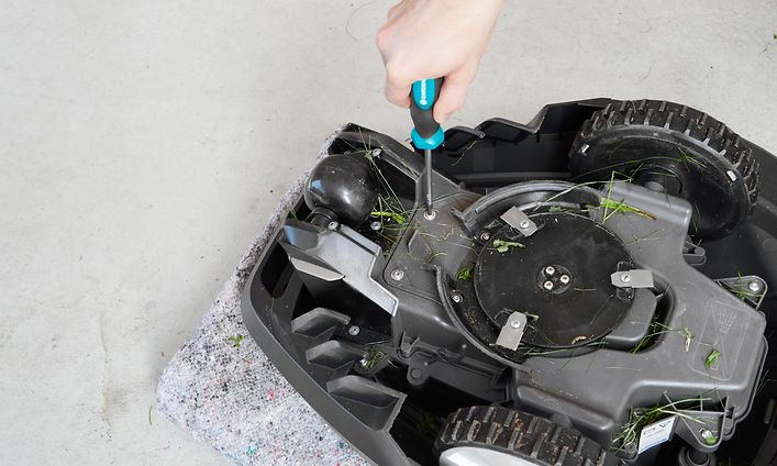 Robottiruohonleikkuri ylösalaisin ja käsi ruuvaamassa sen pohjaa ruuvimeisselillä