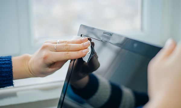 Henkilö pyyhkii liinalla kannettavan tietokoneen näyttöä
