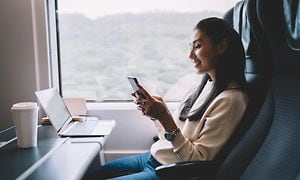 Junassa istuva nainen käyttää puhelintaan sekä kannettavaa tietokonettaan samanaikaisesti