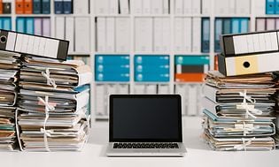 Tietokoneet - Kannettava tietokone asiakirjojen ja paperipinojen keskellä