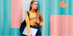 Nainen seisoo värikästä seinää vasten Lenovo Ideapad 5 ja kahvikuppi kädessään