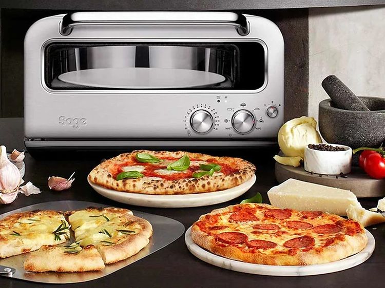 Erilaisia pizzoja pöydällä tarjolla sekä Sage-pizzauuni taustalla
