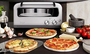Erilaisia pizzoja pöydällä tarjolla sekä Sage-pizzauuni taustalla