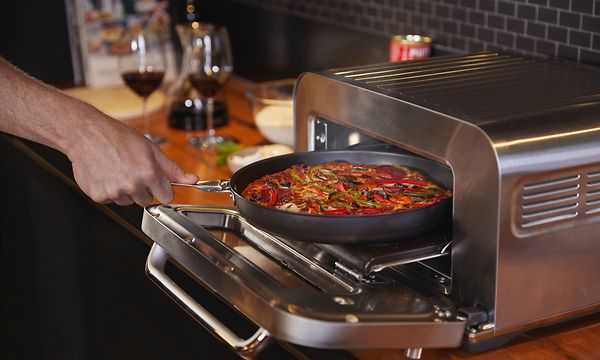 Käsi laittamassa pannullista pizzaa Sage-pizzauuniin sisälle