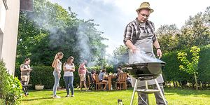 Mies grillaa, taustalla ihmisiä