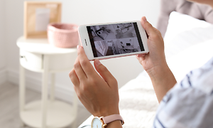 Nainen pitelee iPhonea kädessään ja katselee turvakameran kuvaa sen näytöltä