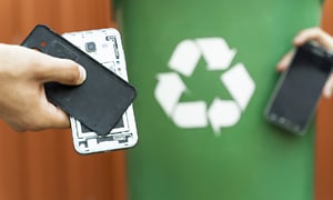 Henkilö viemässä vanhaa rikkonaista älypuhelinta kierrätykseen