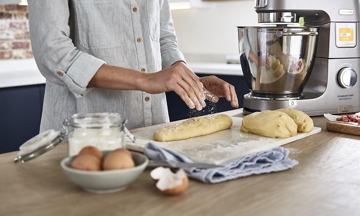 Nainen leipoo leipää keittiössä ja vieressä Kenwood-yleiskone