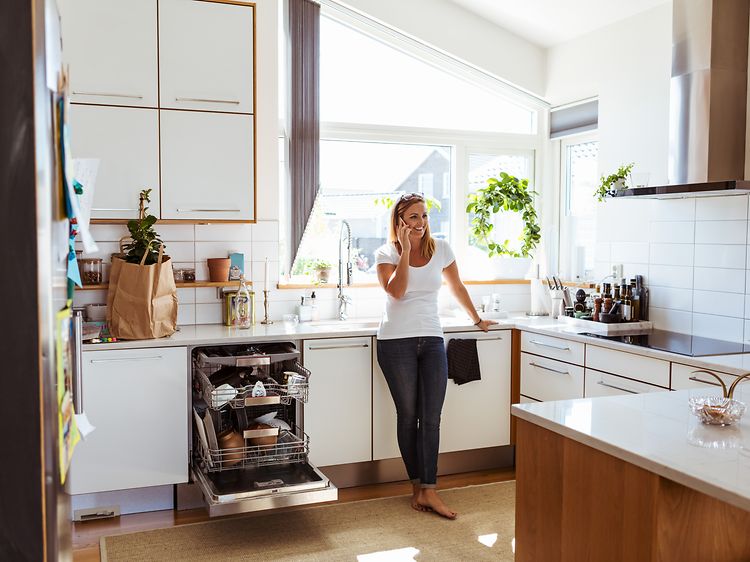 Nainen seisoo ja puhuu puhelimessa keittiössä, jossa on avoin integroitu astianpesukone