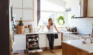 Nainen seisoo ja puhuu puhelimessa keittiössä, jossa on avoin integroitu astianpesukone