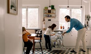 Mies ja lapset ottavat astioita ulos integroidusta astianpesukoneesta