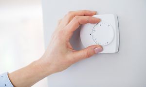 Käsi säätää huoneen seinällä olevaa termostaattia