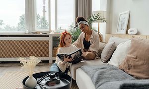 Kaksi naista istuvat sohvalla lukemassa kirjaa, Airthings-ilmanlaatumittari pöydällä heidän takanaan