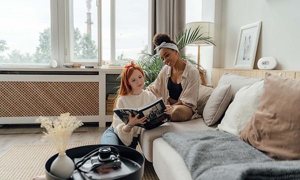 Kaksi naista istuvat sohvalla lukemassa kirjaa, Airthings-ilmanlaatumittari pöydällä heidän takanaan