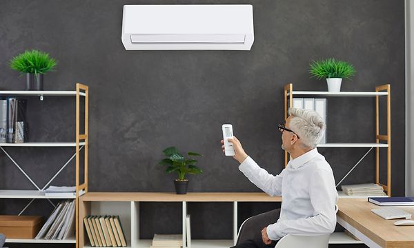 Mies ohjaa kaukosäätimellä kotitoimiston seinällä olevaa ilmalämpöpumppua 