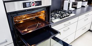 Uuni, joka on avoinna ja uunipellillä on paistolämpömittari