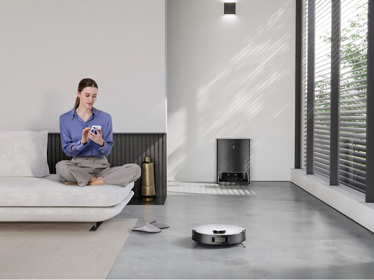 Ecovacs Deebot X1 -puhdistusrobotti sohvalla istuvan naisen vieressä puhdistamassa lattiaa