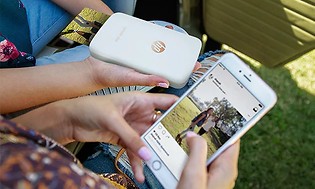 HP Sprocket -tulostin ja älypuhelin henkilöiden kädessä sovelluksen ollessa samalla auki