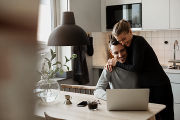 Pariskunta käyttää kannettavaa tietokonetta keittiössä 