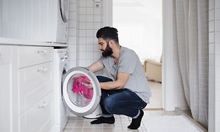 Mies laittaa pyykkiä pyykinpesukoneeseen