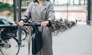 Nainen kulkee sähköpotkulaudalla ja ohjaustangolla roikkuu salkku