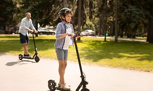 Wearables - Young boy riding electric scooter with father in the background