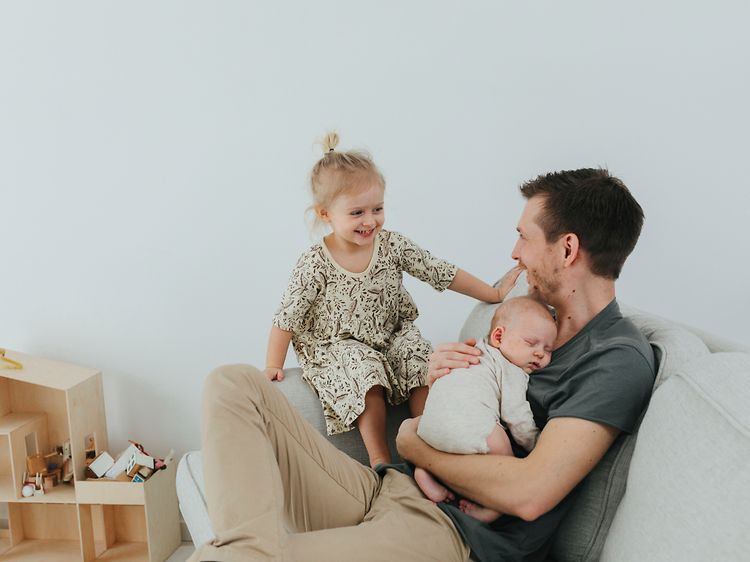 Isä istuu sohvalla yhdessä kahden pienen lapsensa kanssa