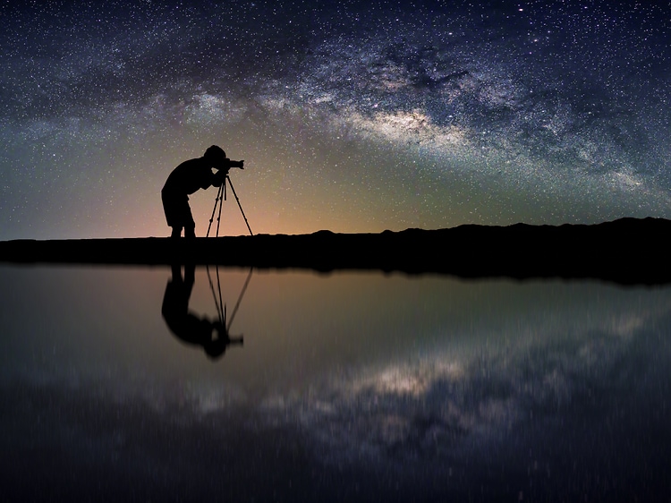 Mies kuvaa kameralla horisonttia tähtitaivas taustalla