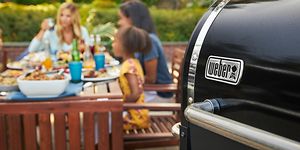 Weber-pellettigrilli ja perhe ruokailemassa taustalla