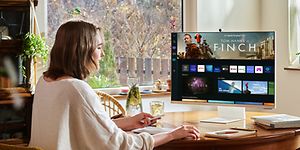 Nainen istuu pöydän ääressä ja selaa suoratoistosisältöä Samsung Smart Monitor -näytöltä